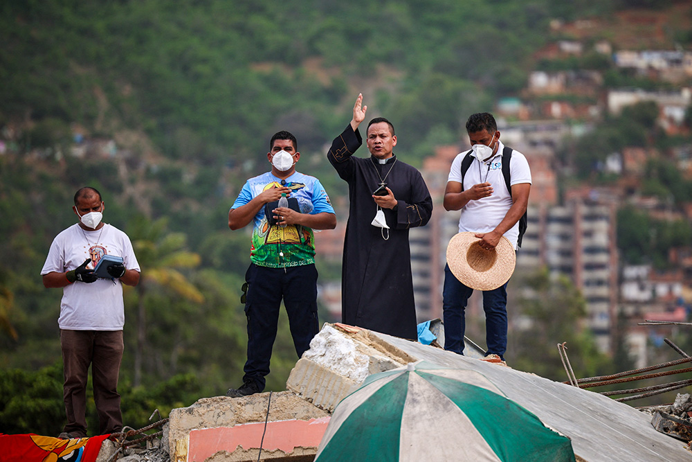 A priest gives a blessing as he stands amid rubble at the site of a collapsed building in La Guaira, Venezuela, July 1, 2026, in the aftermath of earthquakes. (OSV News/Reuters/Adriano Machado)