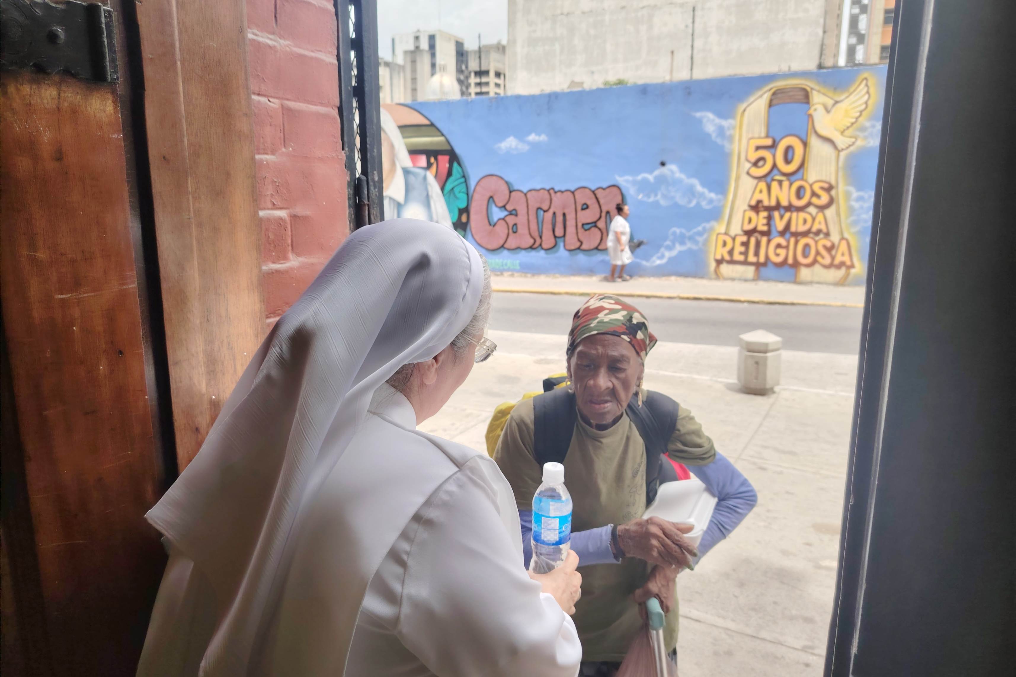 La Hna. Rosa Lozano, de las Siervas de Jesús, entrega alimentos, el 30 de junio de 2026, a una persona damnificada en Caracas. Junto con las otras ocho religiosas de su comunidad, prepara diariamente comidas para las personas afectadas por los terremotos. (Foto: Graciela Portillo)