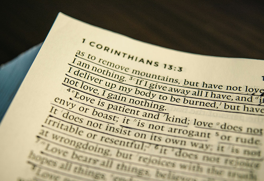 A photo illustration display the top left corner of a Bible, listing "1 Corinthians 13:3" at the top, with about ten lines of verses underneath. (Unsplash/Jonathan Meyer)