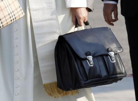 Pope Francis holds his personal bag as he boards a plane.