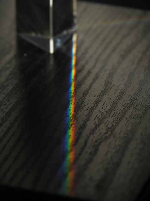 A prism is shown on a dark table, emitting a beam of multicolored light along the table's surface. (Unsplash/Rafael Garcin)