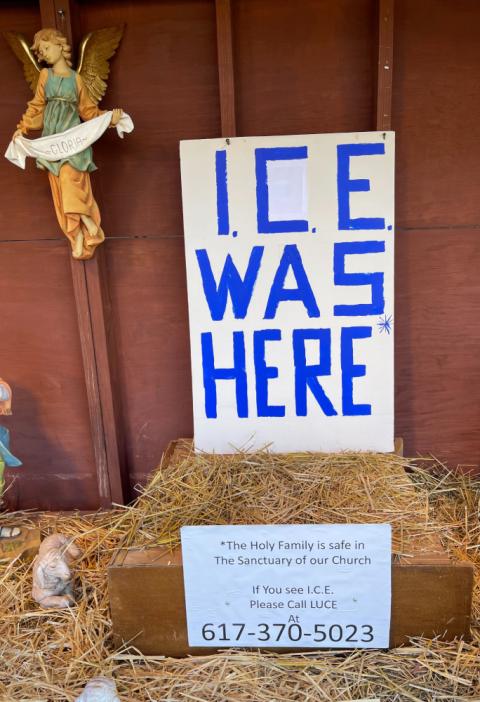 A large sign says, "ICE WAS HERE". "The Holy Family is safe in The Sanctuary of our Church," a smaller sign adds. "If you see ICE, please call LUCE," referring to an immigrant assistance network in Massachusetts.