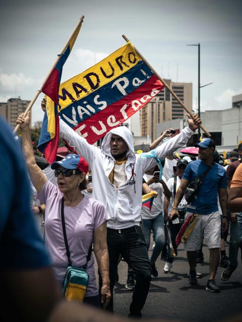 Ciudadanos protestan contra Nicolás Maduro en Venezuela con una pancarta que dice “Maduro vais pa afuera”. La prolongada crisis política del país ha generado años de conflictividad social, polarización y demandas de cambio democrático. (Foto: Pexels/Jhostin Peraza)