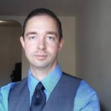 Headshot of David Kovacs from the chest up with a neutral smile and a short haircut in a light blue collared shirt, a navy tie and charcoal grey vest. 