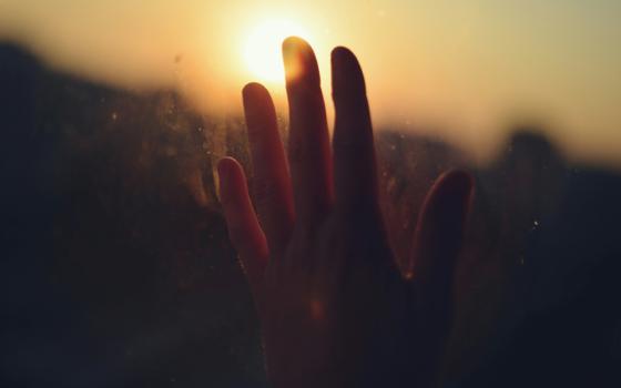 Hand smudging a glass window, backlit by a warm sunset shining through fingers