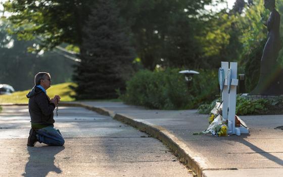 A man prays near crosses outside Annunciation Church in Minneapolis Aug. 28, 2025, following a shooting the previous day. A shooter opened fire with a rifle through the windows of the school's church and struck children attending Mass Aug. 27 during the first week of school, killing two and wounding 17 people in an act of violence the police chief called "absolutely incomprehensible." (OSV News/Reuters/Tim Evans)