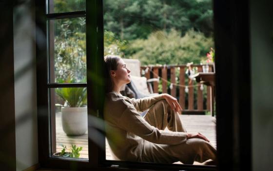 Woman sits by window.