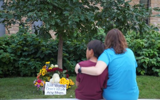 People sit across from a memorial near boarded windows damaged in the Aug. 27 fatal school shooting at Annunciation Catholic Church Aug. 28 in Minneapolis. (AP/Abbie Parr)