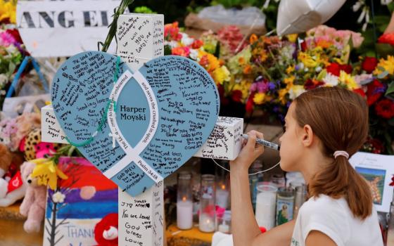 A child writes a message as people visit a makeshift memorial at Annunciation Catholic Church after theAug. 27 fatal shooting at the school on Aug. 29 in Minneapolis. (AP/Bruce Kluckhohn)