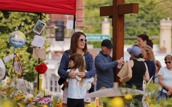 A child is embraced as people visit a makeshift memorial Aug. 29, 2025, at Annunciation Catholic Church in Minneapolis after the Aug. 27 shooting there during a Mass attended by students of the affiliated school. (AP photo/Bruce Kluckhohn)