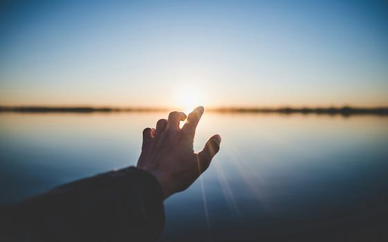 A photo illustration shows a hand outstretched toward a horizon. (Unsplash/Marc-Olivier Jodoin)
