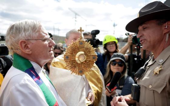 Jesuit Fr. Dan Hartnette speaks with an Illinois State Police officer as members of a Catholic group take part in a procession near the U.S. Immigration and Customs Enforcement Broadview facility in Chicago Oct. 11. The group had hoped to share Communion with detainees at the facility. (OSV News/Jeenah Moon, Reuters)