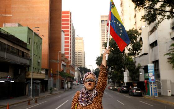 A supporter of Venezuelan President Nicolás Maduro holds a flag of Venezuela on a street near Miraflores Palace in Caracas, Jan. 3, 2026, after U.S. President Donald Trump said the U.S. has struck Venezuela and captured Maduro. (OSV News/Reuters/Leonardo Fernandez Viloria)