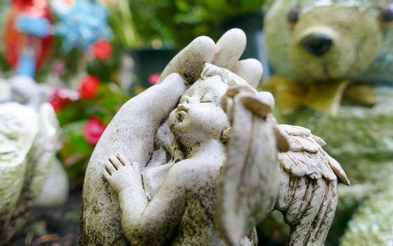 A photo illustration shows a sculpture of an angel child resting in adult hands, pictured in an outdoor setting, perhaps a cemetery. (Pixabay/dominic_winkel)