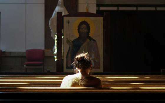 A woman sits in a church pew in front of an icon of Jesus and a statue of Mary (Unsplash/Josh Applegate)