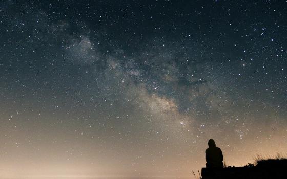 Silhouette of a person sitting on a hill looking at the Milky Way galaxy (Unsplash/Clement Duguerre)