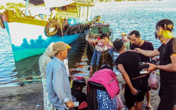 Mary Magdalene Vu Thi Tue (center, in denim jacket) sells fish to customers in Quang Tri, Vietnam, on April 22, 2026. At left is the fishing boat her family recently repaired after years of abandonment following the Formosa disaster. (Reporter in Vietnam)